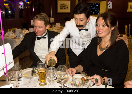 Attore omaggio giocando sfortunato cameriere manuel dalla BBC TV Fawlty Towers serve diners ad una carità divertente funzione Foto Stock