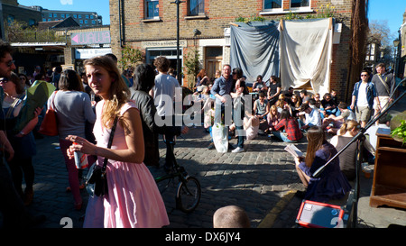 Donna in un abito rosa che cammina in una folla di persone sedute al panificio Jones in Ezra Street Columbia Road Flower Market London E2 Inghilterra UK KATHY DEWITT Foto Stock