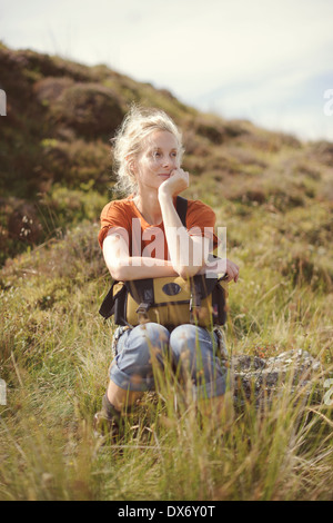Una giovane donna siede tra l'erba su una roccia in campagna Foto Stock
