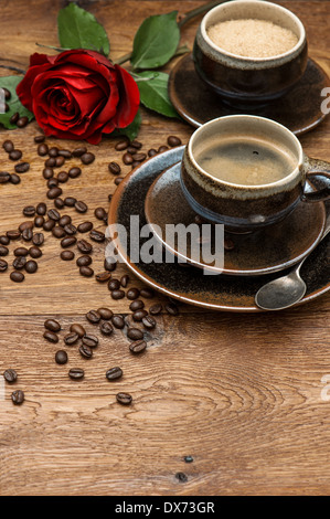 Tazza di caffè nero e rosso fiore rosa su sfondo di legno. Disposizione di festa Foto Stock