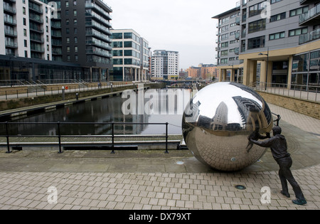 Scultura nel nuovo Dock, precedentemente Clarence Dock, Leeds, che mostra la vita di bronzo di dimensioni figura spinge una sfera di acciaio inossidabile. Foto Stock