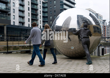 Un giovane a piedi passato una scultura nel nuovo Dock, precedentemente Clarence Dock, Leeds, mostrando una vita in bronzo di dimensioni figura spingendo un inossidabile Foto Stock