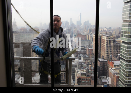 Vista interna di una finestra la rondella in piedi sul ponteggio e fissato mediante cablaggio durante la pulizia di una New York City grattacielo windows Foto Stock