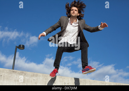 Un giovane maschio modello su un muro di cemento con cielo blu dietro Foto Stock