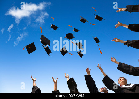 Gli studenti di gettare la laurea cappelli in aria per celebrare con il blu del cielo Foto Stock