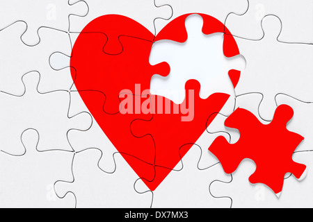 Un cuore rosso puzzle con un pezzo sul lato, una buona immagine per un cuore spezzato, amore, romanticismo e San Valentino temi. Foto Stock