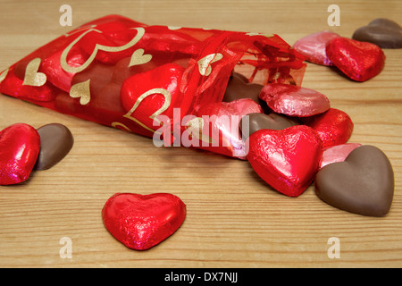 Un sacchetto rosso pieno di a forma di cuore sweetheart cioccolatini riversandosi su di un tavolo di legno. Foto Stock