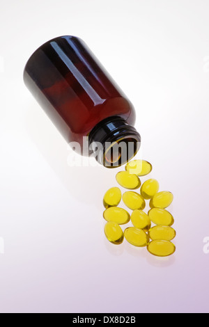 Vitamina capsule fuoriuscita da un flacone su una superficie di colore viola Foto Stock