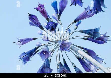 Un "fiore-like' sculture di vetro sospesa su un palo metallico, visto da sotto isolati contro un cielo blu chiaro. Foto Stock