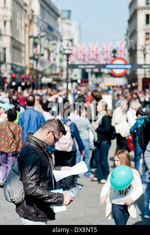 Giovane uomo la lettura di un documento in Piccadilly Circus, Londra Foto Stock