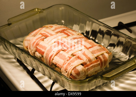 Polpettone crudo avvolto con il bacon in una cesta modello di armatura seduto in un chiaro in Pyrex teglia su una cucina piano cottura Foto Stock