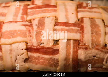 Polpettone crudo avvolto con il bacon in una cesta modello di armatura seduto in un chiaro in Pyrex teglia su una cucina piano cottura Foto Stock