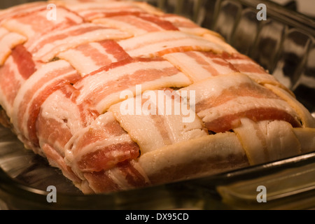 In prossimità di un polpettone crudo avvolto con il bacon in una cesta modello di armatura seduto in un chiaro in Pyrex piatto di cottura di una cucina Foto Stock