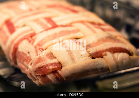 In prossimità di un polpettone crudo avvolto con il bacon in una cesta modello di armatura seduto in un chiaro in Pyrex piatto di cottura di una cucina Foto Stock