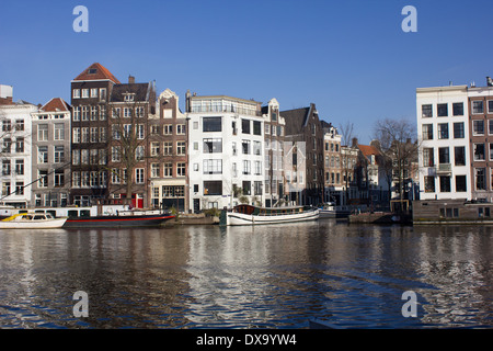 Dutch Canal barche in riflessioni con i tradizionali magazzini sulla giornata di primavera Amsterdam Paesi Bassi Foto Stock