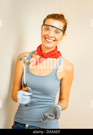 Giovane donna con un martello in mani guardando la fotocamera e sorridente. Foto Stock