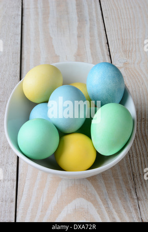 Angolo di Alta Vista del pastello di uova di pasqua in una ciotola. Il bianco la coppa è piena di giallo, verde e blu uova tinto Foto Stock