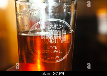 Un parzialmente vuoto in vetro stampato di elementi taglienti Doom Bar real ale retroilluminato in un vetro inciso, pub tavola bicchieri di bevande Foto Stock