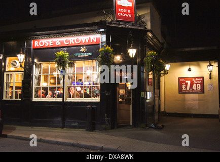 Esterno della Greene King Pub Rose & Crown, Woodford Green, Essex, Inghilterra di notte guardando attraverso la finestra Foto Stock