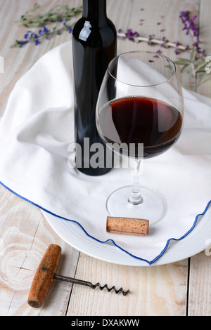 Elevato angolo di vino fiore e ancora in vita. Bicchiere di vino rosso e una bottiglia su un asciugamano e legno tavolo rustico. Formato verticale. Foto Stock