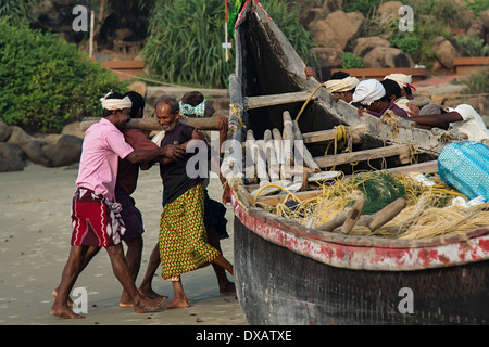 I pescatori a spostare le loro barche da pesca in mare al Lighthouse Beach in Kovalam Kerala, India Foto Stock