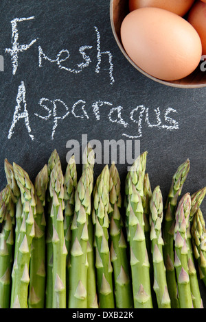 Freschi di punte di asparagi verdi e ampio intervallo libero le uova nella ciotola di legno contro lo sfondo di ardesia, REGNO UNITO Foto Stock