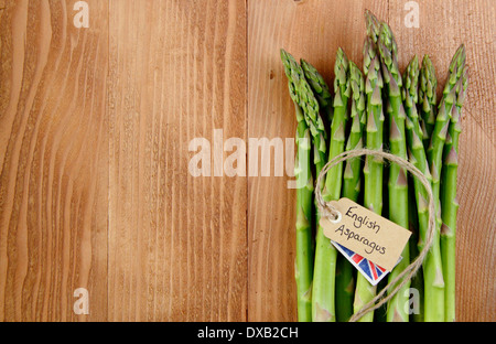 Un grappolo spargolo freschi Asparagi verdi peduncoli con etichetta contro rustico, vintage Sfondo legno, Regno Unito - con copia spazio. Foto Stock