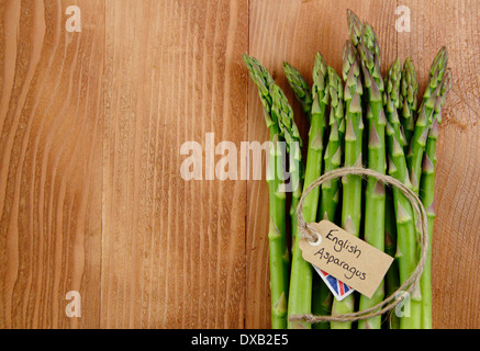 Un grappolo spargolo freschi Asparagi verdi peduncoli con etichetta contro rustico, vintage Sfondo legno, Regno Unito - con copia spazio. Foto Stock