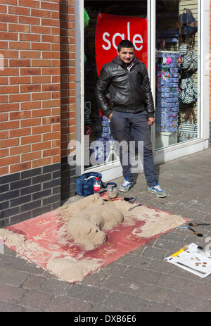 L'artista di strada in un centro commerciale con la sua scultura di sabbia di due cani Foto Stock