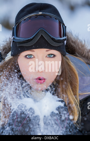 Bella giovane donna tenendo la neve nelle sue mani e soffiare via con una lenta velocità otturatore Foto Stock