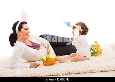 Felice madre e bambino ragazzo con orecchie di coniglietto seduto sul tappeto con cesto di Pasqua Foto Stock