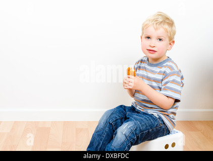 Carino piccolo ragazzo mangiare deliziosa cookie seduto su uno sgabello a casa Foto Stock