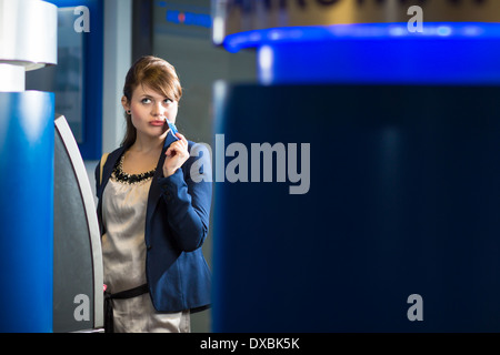 Piuttosto, giovane donna il ritiro di denaro dalla sua carta di credito presso uno sportello ATM (SHALLOW DOF; dai toni di colore immagine) Foto Stock