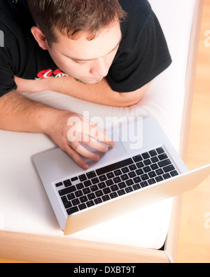 Giovane uomo nel letto con il computer portatile durante la navigazione in internet Foto Stock