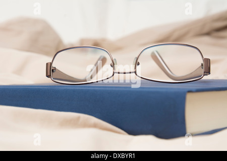 Dettaglio foto che mostra un paio di occhiali e un libro seduti sul letto Foto Stock