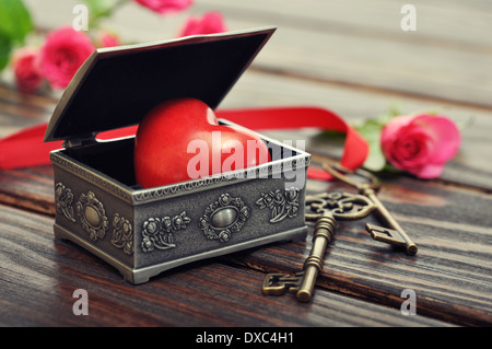 Il cuore di pietra nel vintage scatola regalo con le chiavi e le rose su sfondo di legno Foto Stock