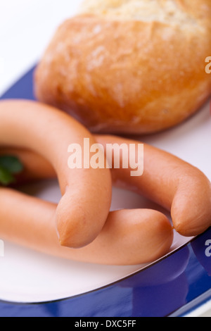 Tre freddo affumicato würstel o salsicce viennesi servita su una piastra con un tuffo in una piccola ciotola e fette di pomodori ciliegia su una bianca di sfondo per studio Foto Stock