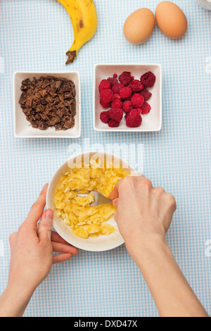 Schiacciamento mani banana close up su un tavolo da cucina. Altri ingredienti torta sul tavolo: uova, lamponi e cioccolato. Foto Stock