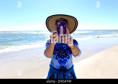 Una donna prendendo immagini o fotografie a una spiaggia con un IPod o un IPhone o un telefono con fotocamera Foto Stock