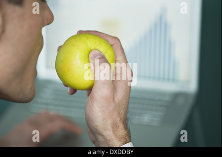 Imprenditore mangiare Apple a un computer portatile con grafico a barre Foto Stock
