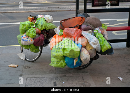 Le persone senza fissa dimora beni mondani in sacchetti di plastica appeso di una bicicletta a Londra Fermata Bus Foto Stock