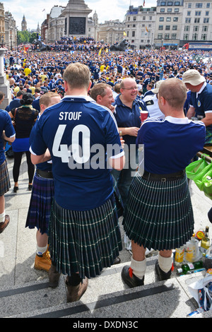 Vista posteriore di due tifosi di calcio scozzesi che indossano i kilt nell'affollata e soleggiata Trafalgar Square, prima di passare alla partita internazionale a Wembley, Inghilterra, Regno Unito Foto Stock