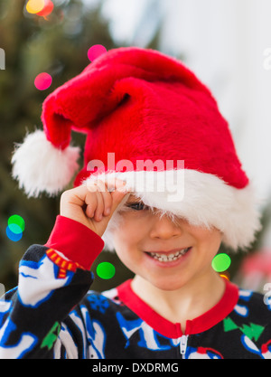 Ragazzo (6-7) peeking attraverso santa hat Foto Stock