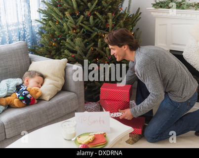L uomo dando presenta sotto albero di Natale mentre suo figlio (6-7) dormire Foto Stock