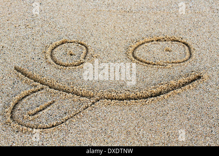 Una faccina sorridente disegno su una spiaggia di sabbia. Foto Stock