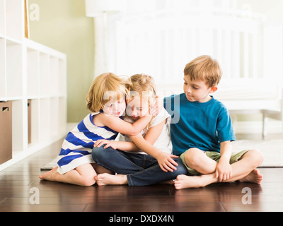 Le ragazze (4-5, 6-7) e ragazzo (8-9) seduto sul pavimento e abbracciando Foto Stock