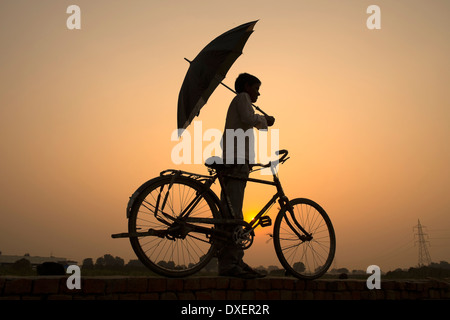 India, Uttar Pradesh, Agra, silhouette di boy holding ombrello accanto alla bici al tramonto Foto Stock