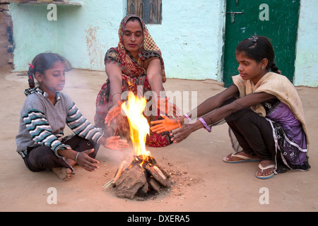 India, Uttar Pradesh, Agra, moglie e due figlie riscalda le loro mani accanto a un piccolo incendio alimentato da sterco di vacca e bambù Foto Stock