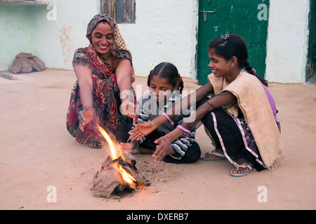 India, Uttar Pradesh, Agra, moglie e due figlie riscalda le loro mani accanto a un piccolo incendio alimentato da sterco di vacca e bambù Foto Stock