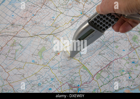 Close up donna di mano che tiene la distanza finder strumento di misurazione su un Ordnance Survey map Foto Stock